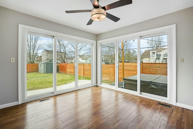 unfurnished sunroom featuring visible vents, a healthy amount of sunlight, and ceiling fan