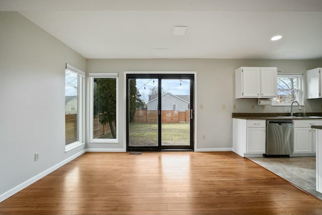 kitchen with a sink, light wood-type flooring, stainless steel dishwasher, and white cabinets