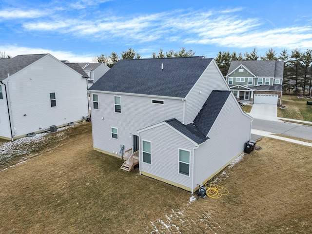 rear view of house with cooling unit, a residential view, a lawn, and roof with shingles