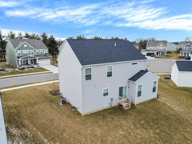 back of property featuring a residential view, a lawn, central AC unit, and a shingled roof