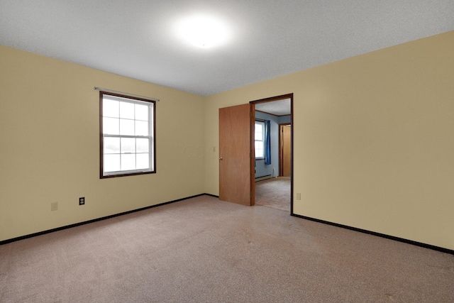 unfurnished room featuring light carpet, a baseboard heating unit, and baseboards