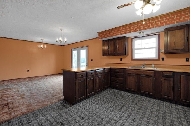 kitchen with a textured ceiling, dark brown cabinetry, a peninsula, a sink, and light countertops