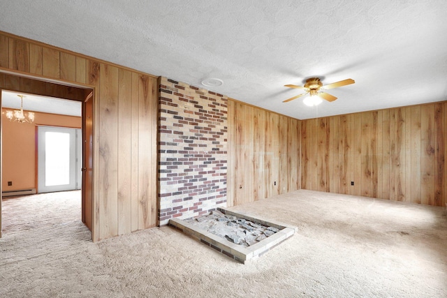 unfurnished room with baseboard heating, a textured ceiling, carpet floors, wood walls, and ceiling fan with notable chandelier