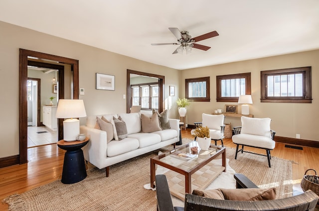 living area with baseboards, a healthy amount of sunlight, ceiling fan, and light wood finished floors