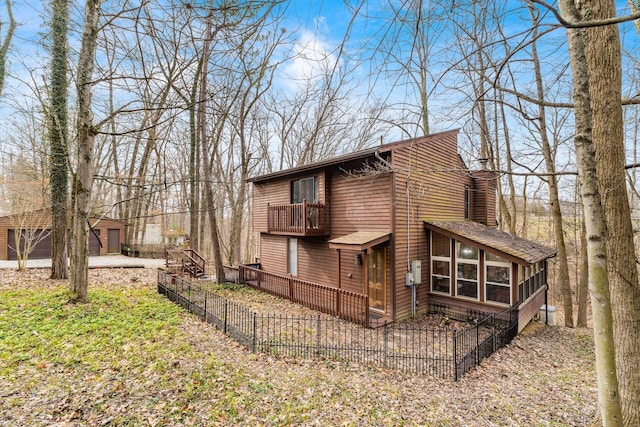 exterior space featuring a balcony, fence, a sunroom, a chimney, and an outdoor structure