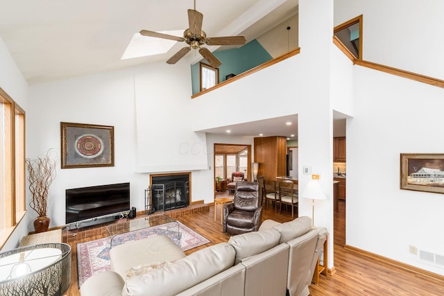 living room featuring visible vents, a fireplace with raised hearth, ceiling fan, light wood-style floors, and lofted ceiling with skylight