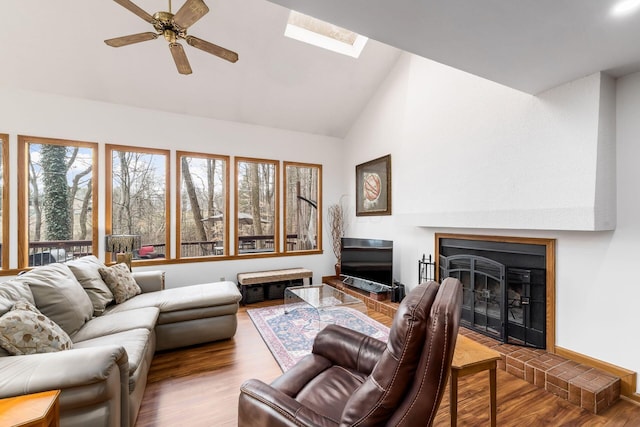 living room with wood finished floors, high vaulted ceiling, a skylight, a fireplace, and ceiling fan