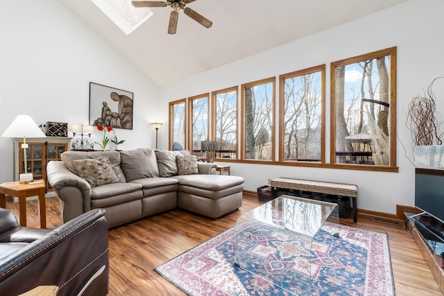 living room featuring baseboards, a skylight, wood finished floors, high vaulted ceiling, and a ceiling fan