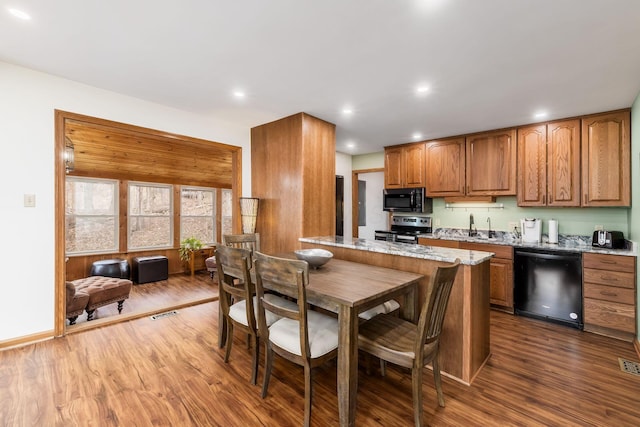 kitchen with brown cabinets, black appliances, dark wood finished floors, and light stone countertops