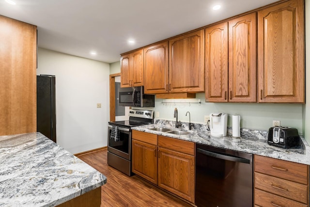 kitchen featuring light stone countertops, dark wood finished floors, brown cabinetry, stainless steel appliances, and a sink