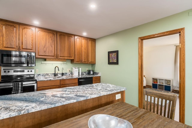 kitchen featuring brown cabinetry, light stone countertops, stainless steel appliances, and a sink