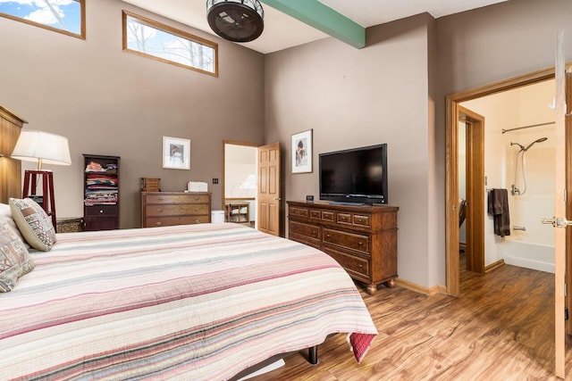 bedroom featuring beam ceiling, light wood-type flooring, baseboards, and a towering ceiling