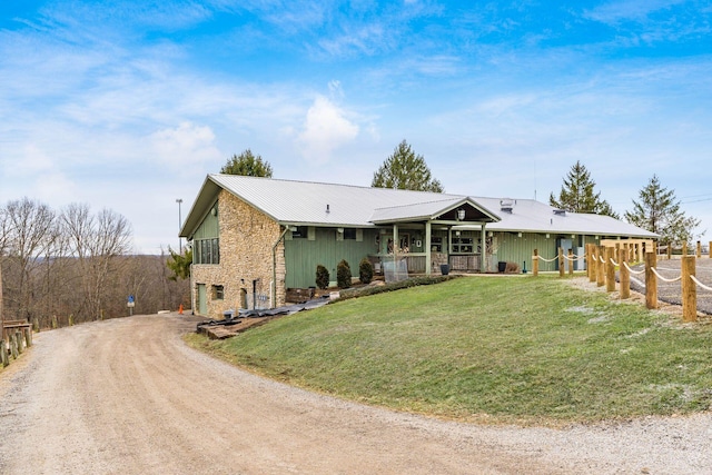 ranch-style house with driveway, stone siding, covered porch, a front yard, and metal roof