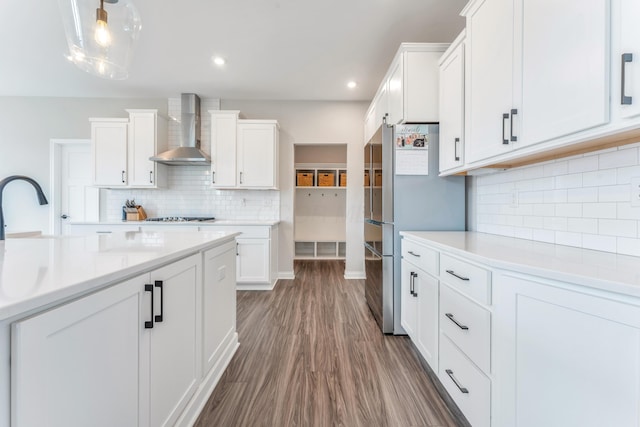 kitchen with white cabinets, wood finished floors, light countertops, and wall chimney range hood