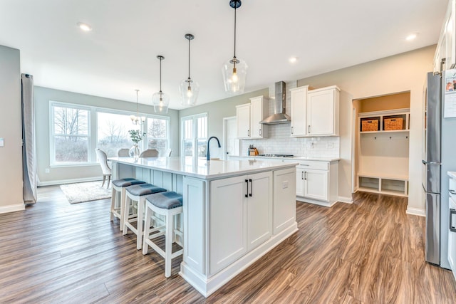 kitchen with tasteful backsplash, light countertops, wood finished floors, white cabinetry, and wall chimney exhaust hood