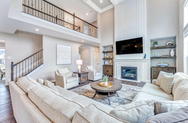 living room featuring a glass covered fireplace, stairway, a towering ceiling, and wood finished floors