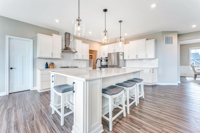 kitchen with visible vents, wall chimney range hood, a kitchen breakfast bar, freestanding refrigerator, and white cabinets