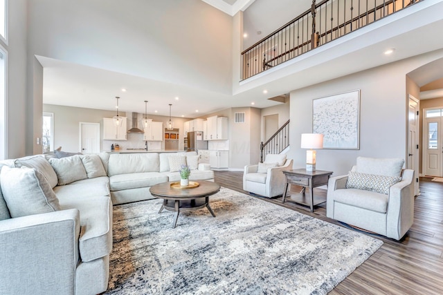 living room with stairs, baseboards, light wood-style flooring, and a towering ceiling