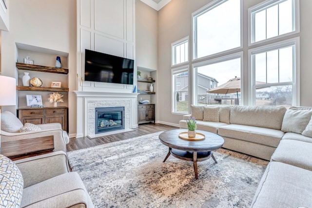 living area featuring built in shelves, wood finished floors, a high ceiling, a stone fireplace, and baseboards