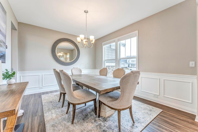 dining space featuring dark wood finished floors, a decorative wall, a notable chandelier, and wainscoting