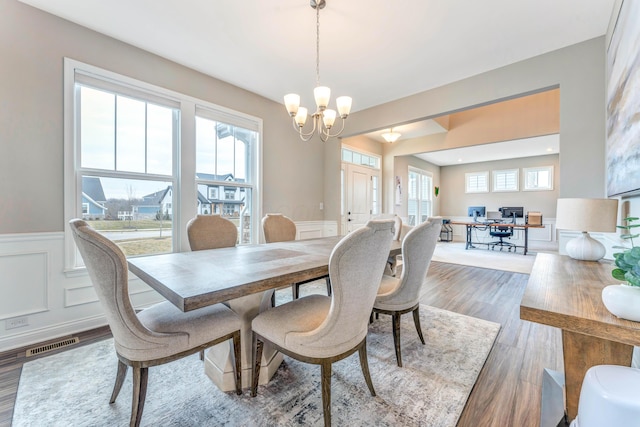 dining area featuring wood finished floors, a wainscoted wall, visible vents, a decorative wall, and a chandelier