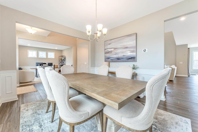 dining room with a wainscoted wall, a notable chandelier, wood finished floors, and a decorative wall