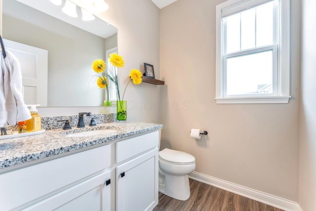 half bath with baseboards, toilet, wood finished floors, and vanity