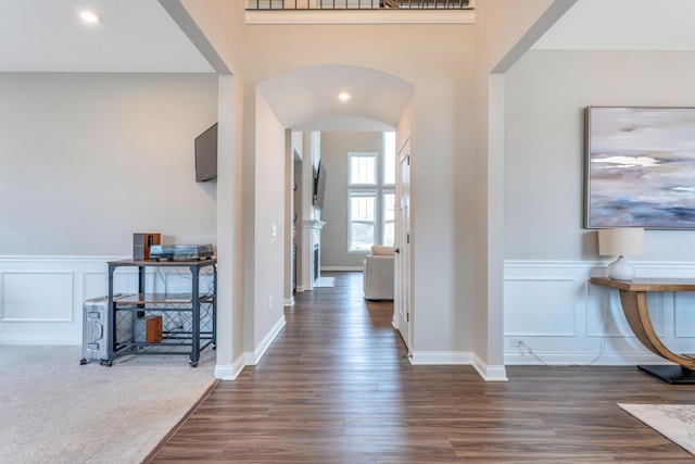 entryway featuring dark wood-style flooring, wainscoting, arched walkways, a decorative wall, and dark colored carpet