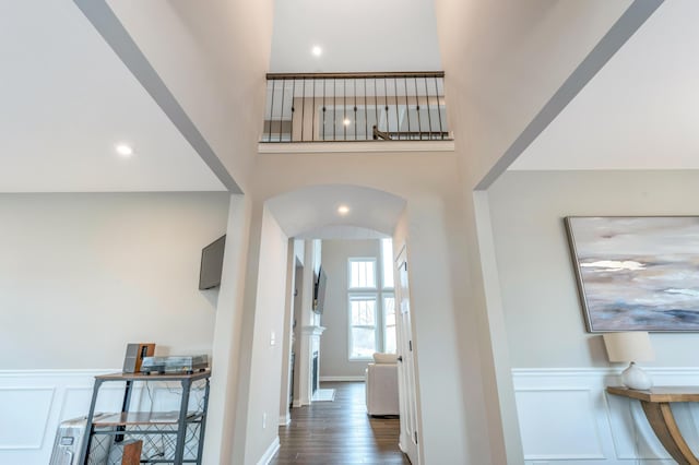 hallway featuring a decorative wall, wood finished floors, arched walkways, and wainscoting