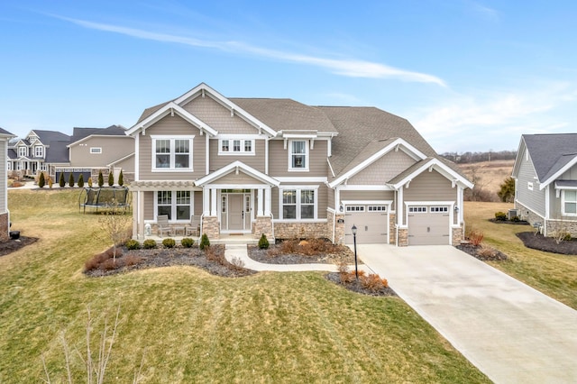 craftsman-style house featuring driveway, a front lawn, a garage, stone siding, and a trampoline