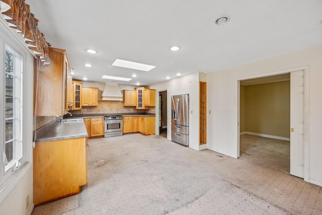 kitchen with a skylight, a sink, stainless steel appliances, custom range hood, and tasteful backsplash