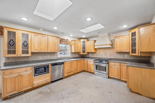 kitchen featuring custom range hood, a sink, dark countertops, appliances with stainless steel finishes, and a skylight