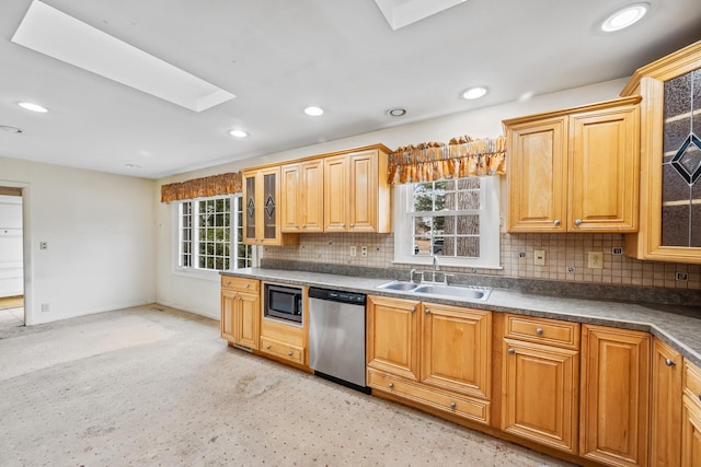 kitchen with a skylight, built in microwave, a sink, decorative backsplash, and stainless steel dishwasher