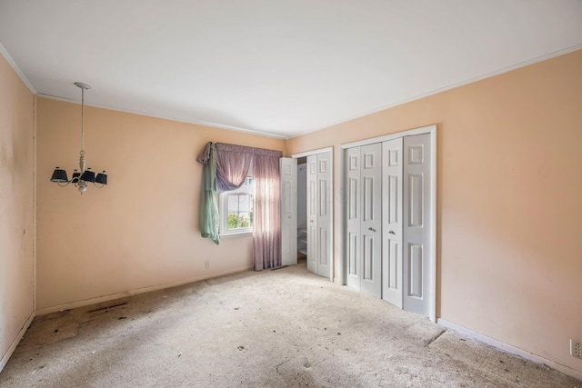 unfurnished bedroom with crown molding, a notable chandelier, multiple closets, and carpet floors