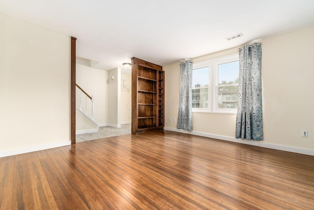 unfurnished living room with visible vents, stairway, baseboards, and wood finished floors