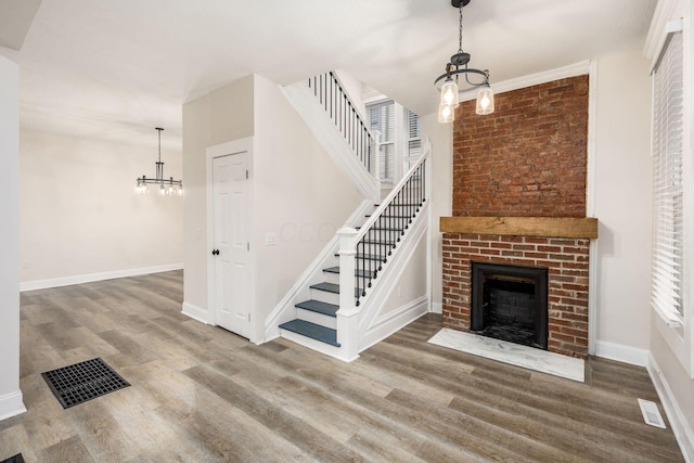 unfurnished living room with visible vents, a brick fireplace, baseboards, wood finished floors, and a notable chandelier