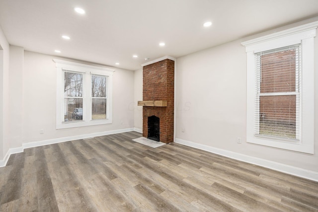 unfurnished living room with recessed lighting, baseboards, a brick fireplace, and wood finished floors