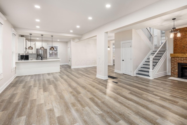 unfurnished living room with a brick fireplace, baseboards, stairs, recessed lighting, and light wood-style floors