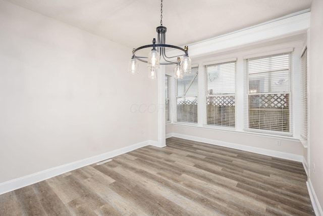 unfurnished dining area featuring a notable chandelier, baseboards, and wood finished floors