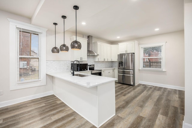 kitchen with a peninsula, a sink, stainless steel appliances, wall chimney range hood, and backsplash