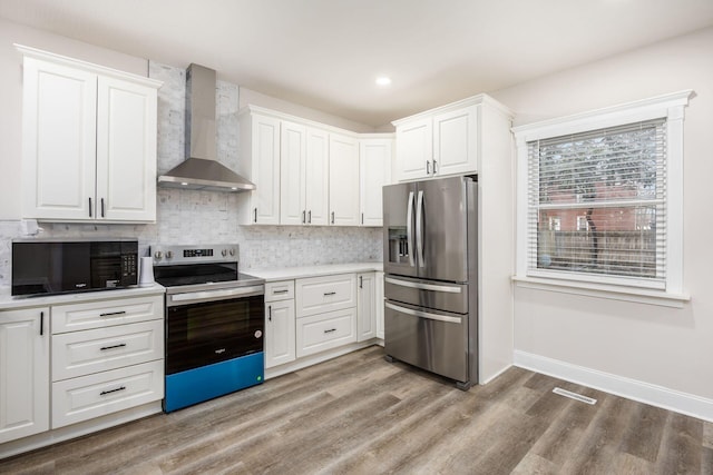 kitchen with light wood-type flooring, stainless steel appliances, light countertops, and wall chimney range hood