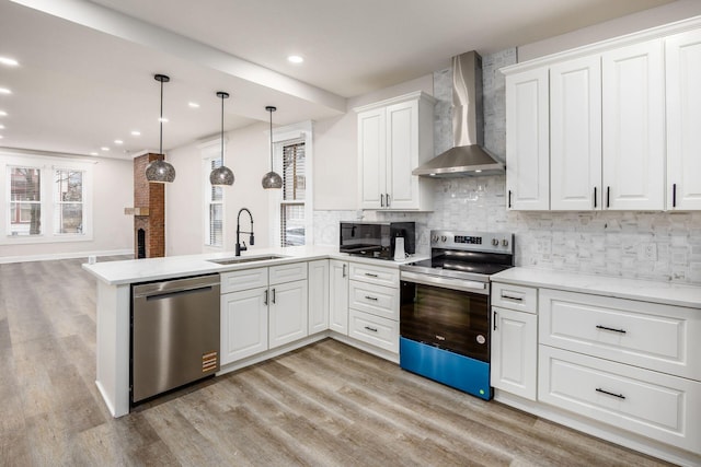 kitchen featuring a peninsula, a sink, appliances with stainless steel finishes, wall chimney range hood, and tasteful backsplash