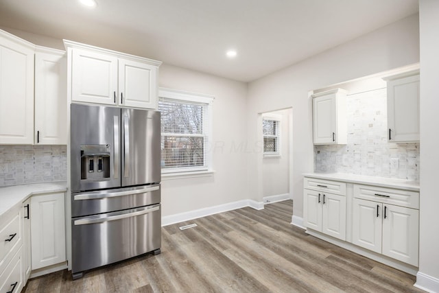 kitchen with baseboards, light wood-type flooring, light countertops, stainless steel refrigerator with ice dispenser, and white cabinetry