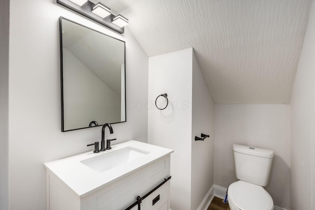 bathroom featuring baseboards, toilet, vanity, and lofted ceiling