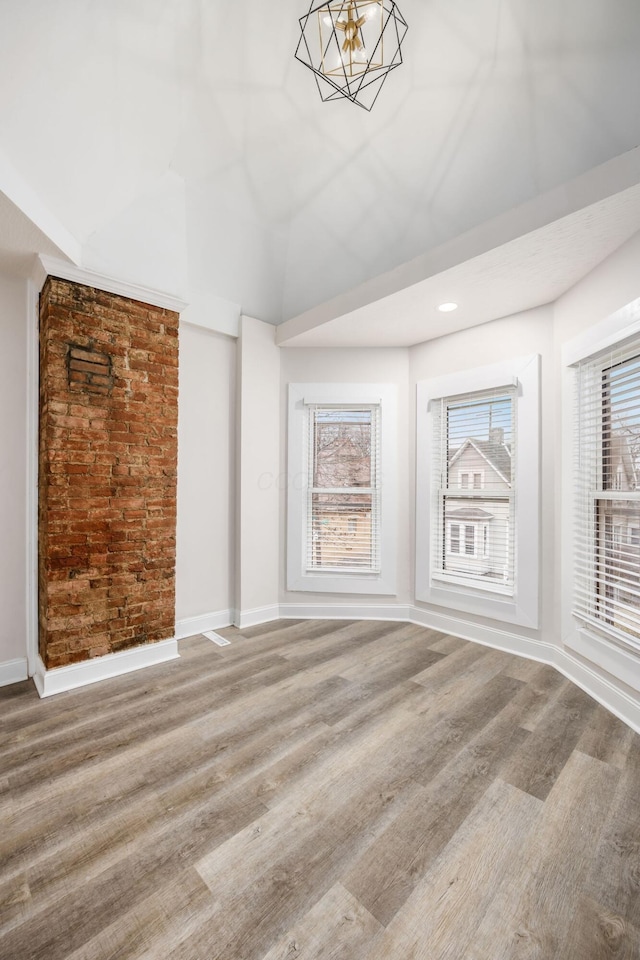 spare room featuring a chandelier, baseboards, and wood finished floors