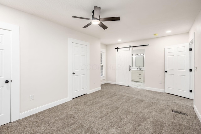 unfurnished bedroom featuring ensuite bathroom, a sink, a barn door, carpet, and baseboards