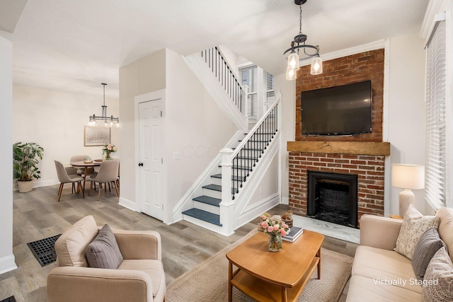 living room with wood finished floors, stairway, an inviting chandelier, a fireplace, and baseboards