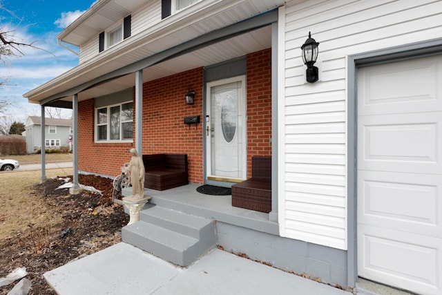 doorway to property with brick siding, covered porch, and an attached garage