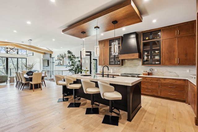 kitchen featuring light countertops, tasteful backsplash, premium range hood, and a sink