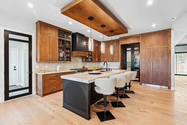 kitchen with custom exhaust hood, light wood-style floors, brown cabinets, and light countertops